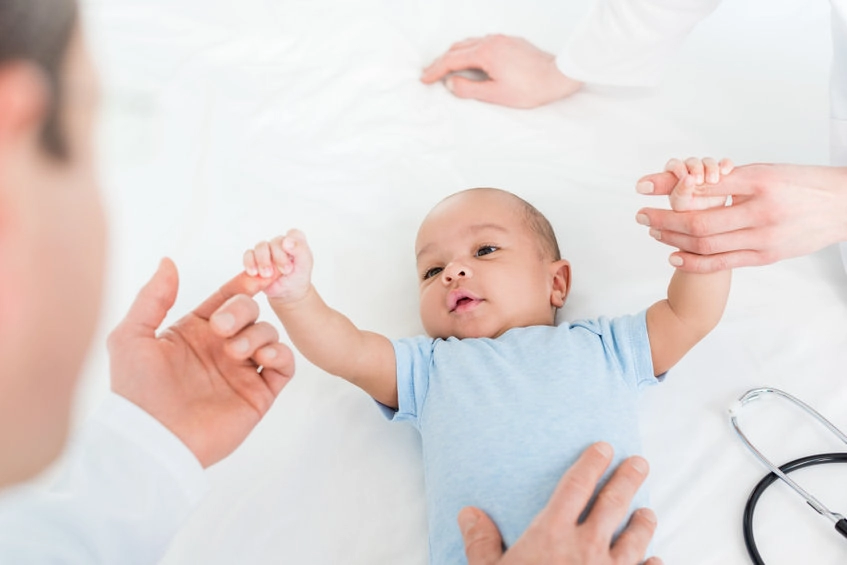 Pediatricians tickling little baby on bed