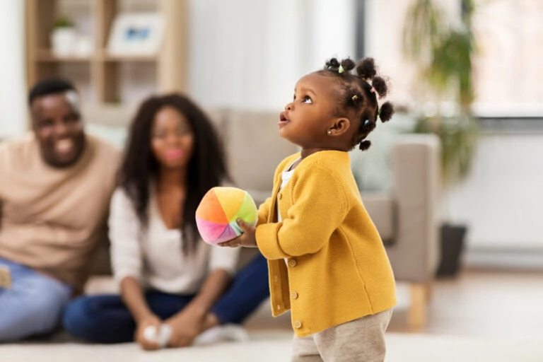 african american baby girl playing with ball and parents at home